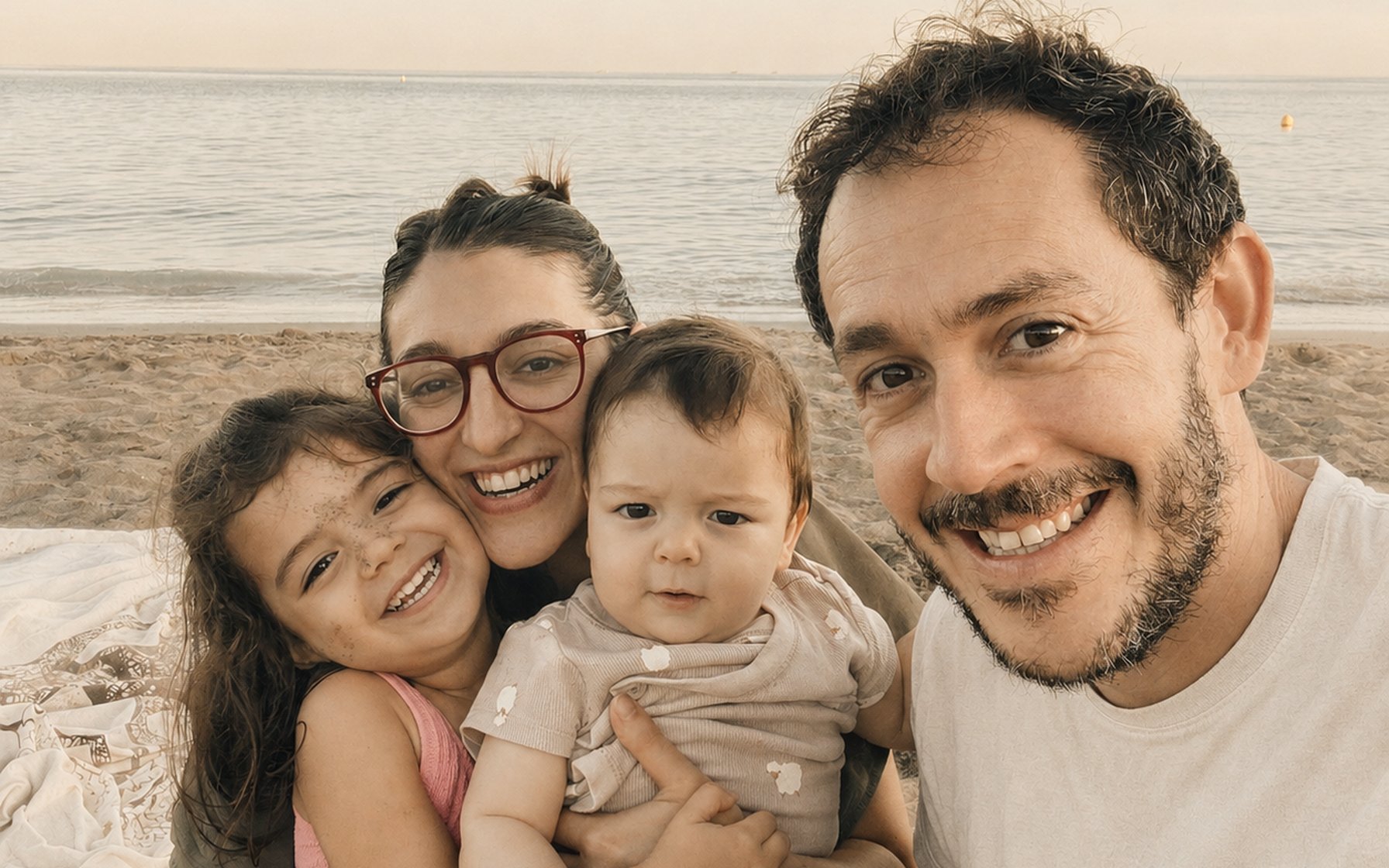 A family of four together on a Costa del Sol beach at sunset, the young daughter and baby smiling in their parents’ arms